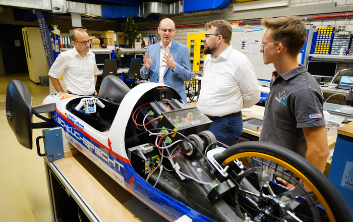 Claus Fleig, Stephan Trahasch, Martin Gassner-Herz und ein Student stehen hinter einem Fahrzeug ohne Motohaube und reden.