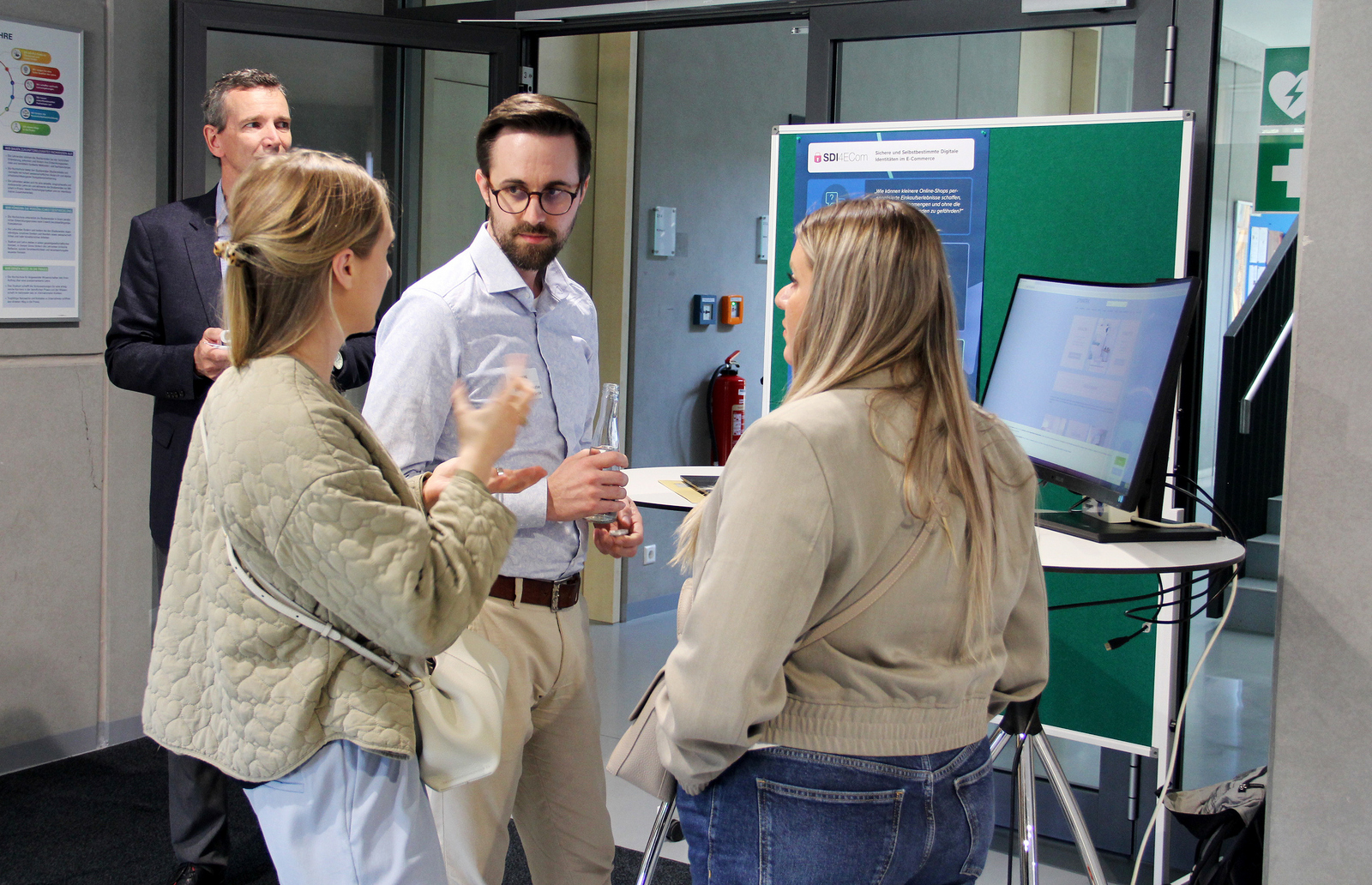 Ein Mann und zwei Frauen stehen an einem Stand im Foyer und unterhalten sich