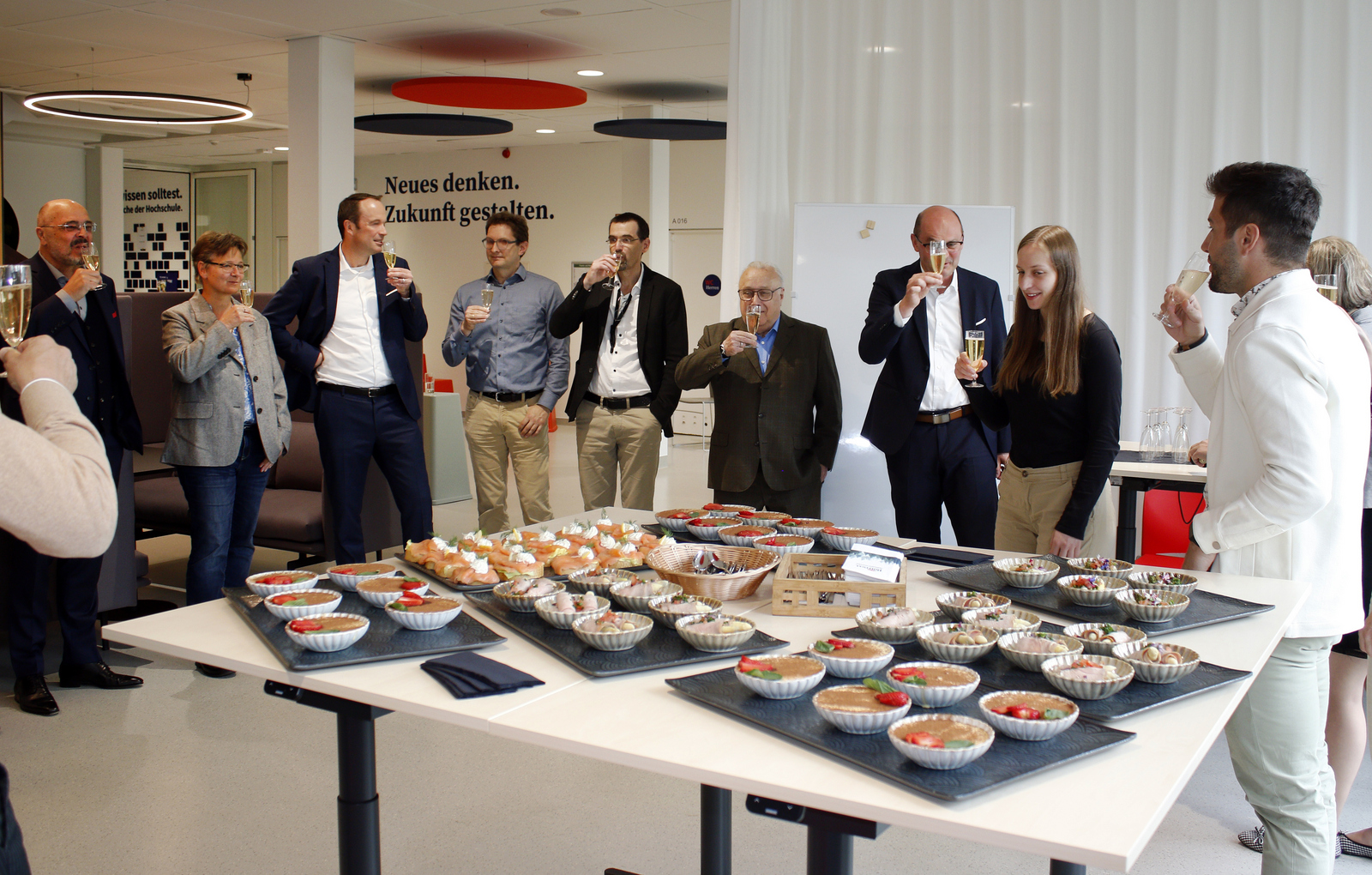 Die Gäste stehen um ein Tisch mit Häppchen herum und stoßen an