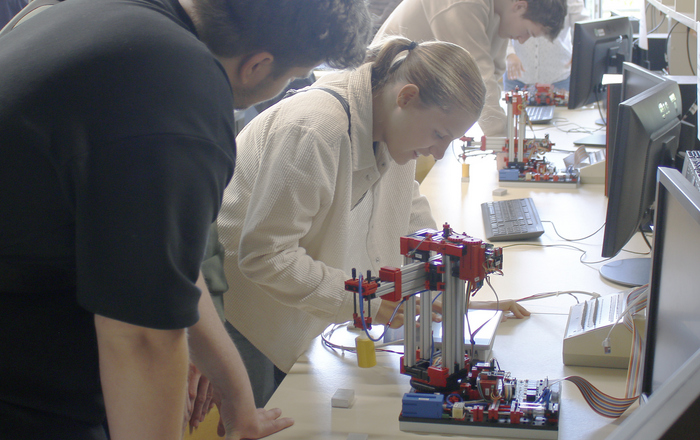 An einem Tisch im Labor basteln zahlreiche Menschen an Kranmodellen