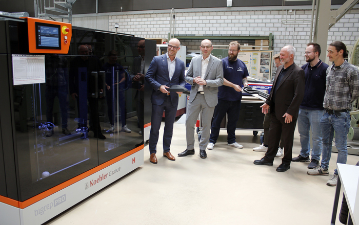 Die Personen stehen neben dem 3D-Drucker und vor dem Schluckpecht und präsentieren eine Fahrzeugsilhouette und einen Streckenverlauf aus dem 3D-Drucker.