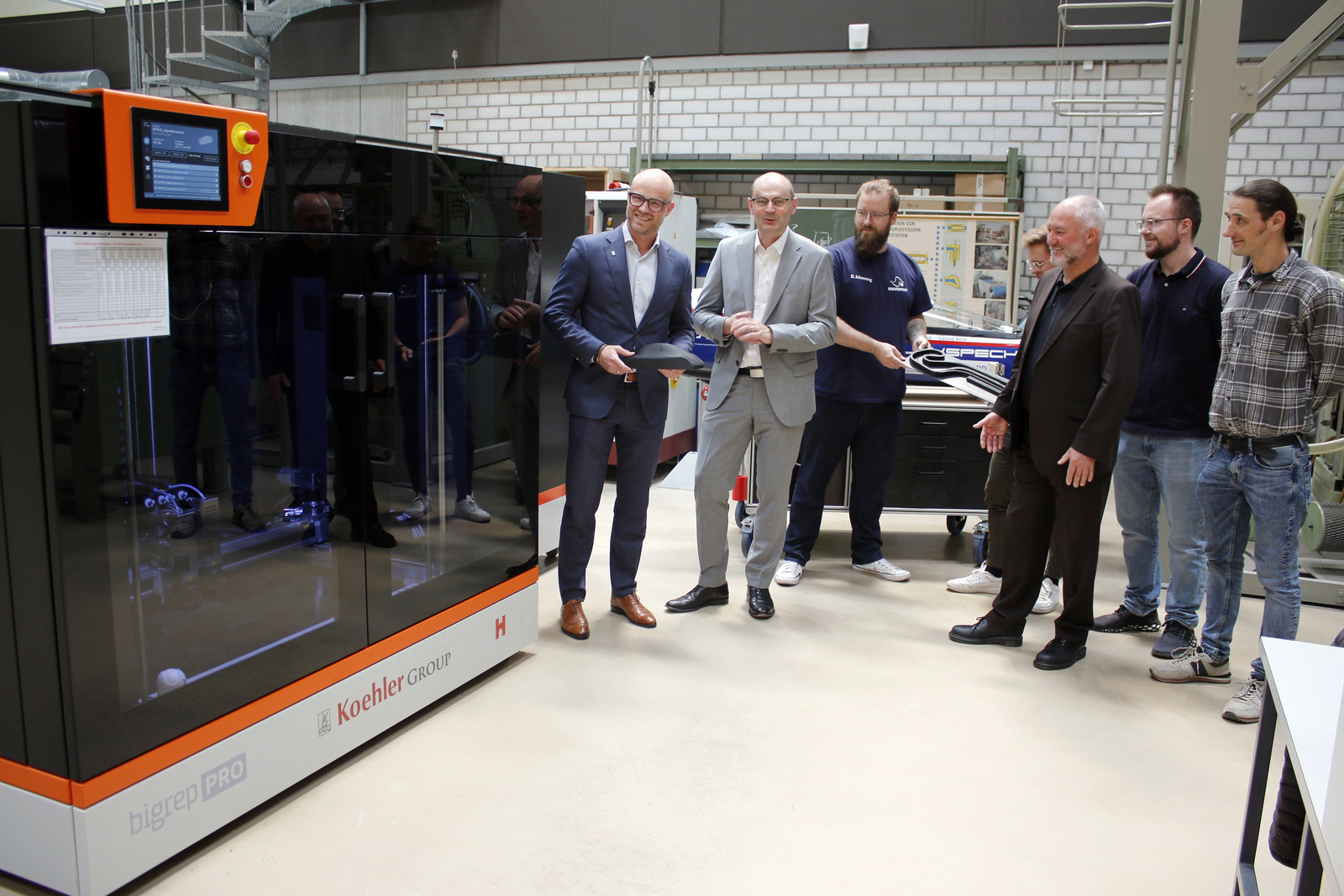 Die Personen stehen neben dem 3D-Drucker und vor dem Schluckpecht und präsentieren eine Fahrzeugsilhouette und einen Streckenverlauf aus dem 3D-Drucker.