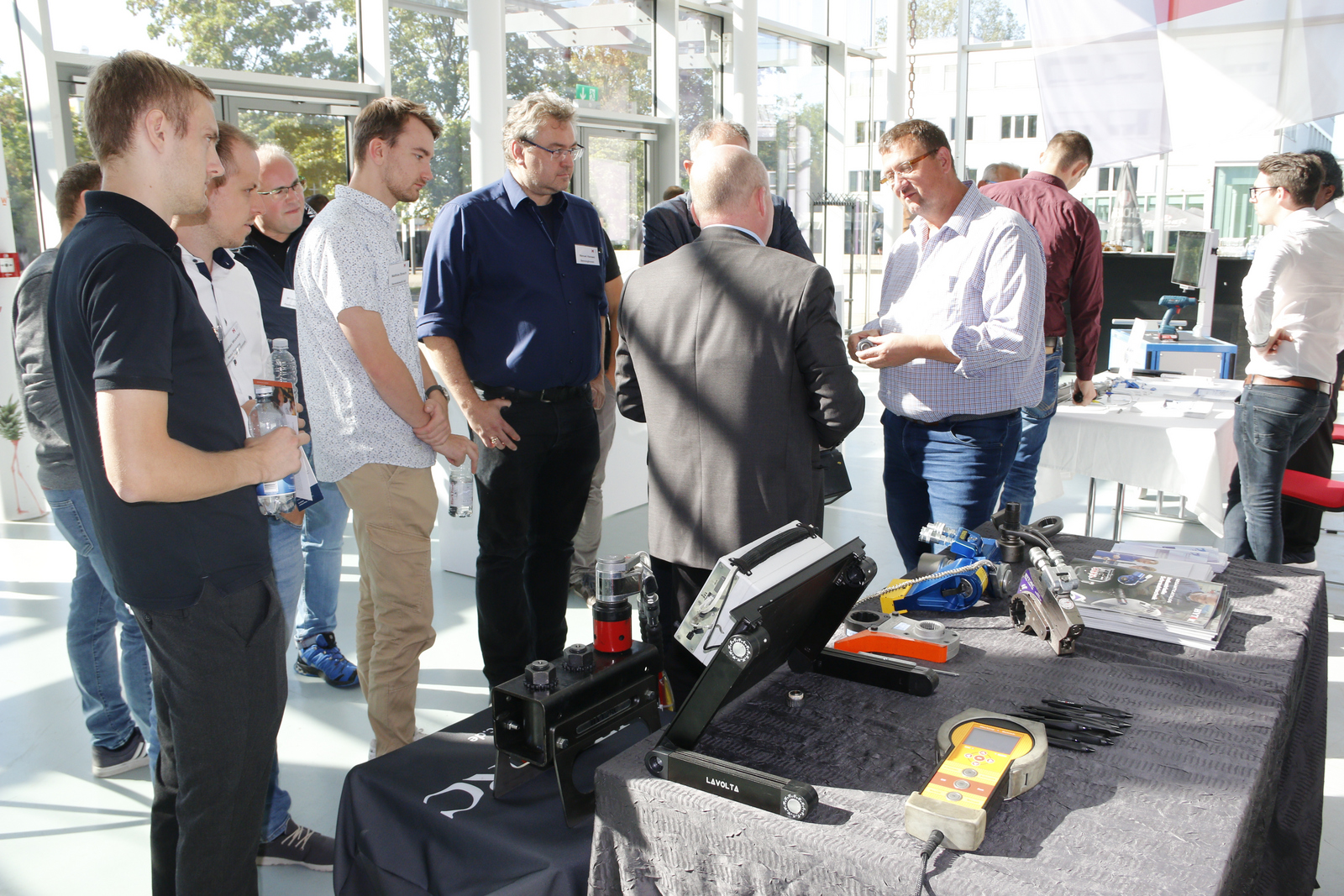 Gruppe von Männer im Foyer, einer hält eine Schraube in der Hand und ein anderer erklärt etwas