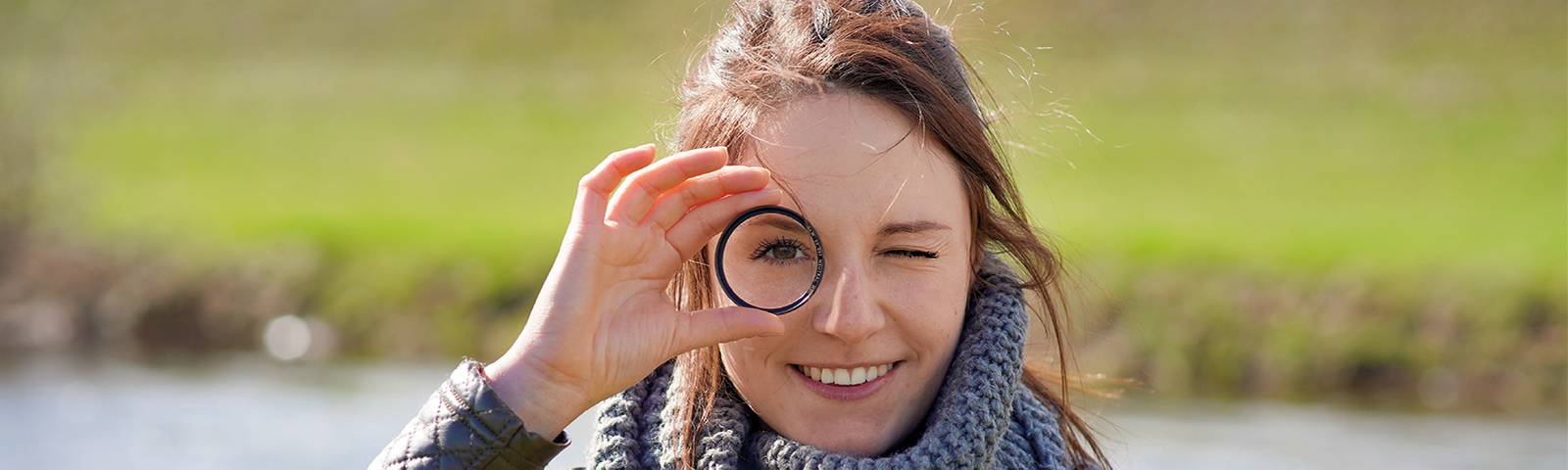 Frau blickt durch eine Linse lächelnd in die Kamera
