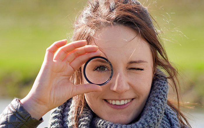 Frau blickt durch eine Linse lächelnd in die Kamera