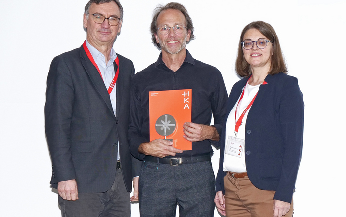 Zwei Männer und eine Frau stehen nebeneinander, der Mann in der Mitte hält eine Urkunde in den Händen 