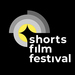 Logo des shorts film festivals in den Fraben scharz weiß grau und gelb deutet durch mehre ineinander liegende Halbkreise und Kreise ein Kameralinse an in deren unterer  rechter Ecke untereinander die Wort shorts film festival stehen 