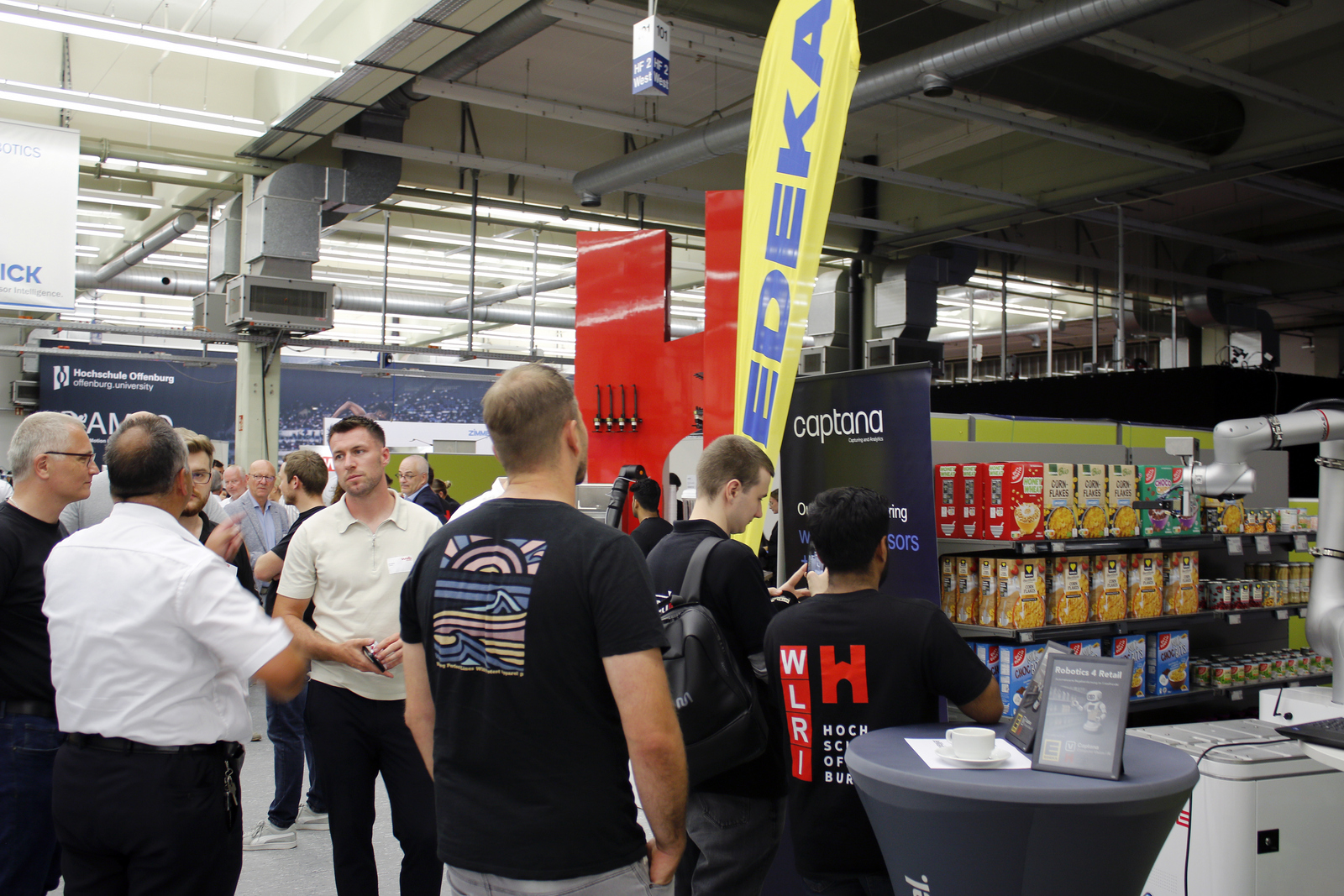 Mehrere menschen beobachten wie ein Roboter etwas in einem Supermarktregal greift