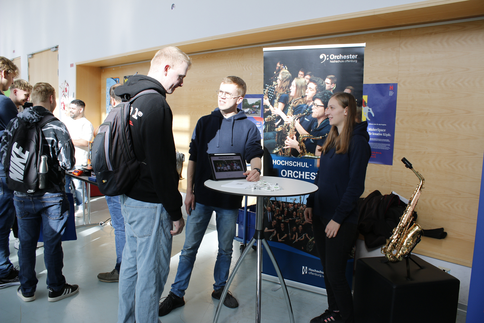 Drei  junge Leute unterhalten sich am Infotisch von Hochschulorchester und -chor