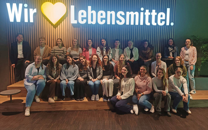 Gruppenfot von WP6-Studierende unter dem leuchtenden Edeka-Schriftzug "Wir lieben Lebensmittel"
