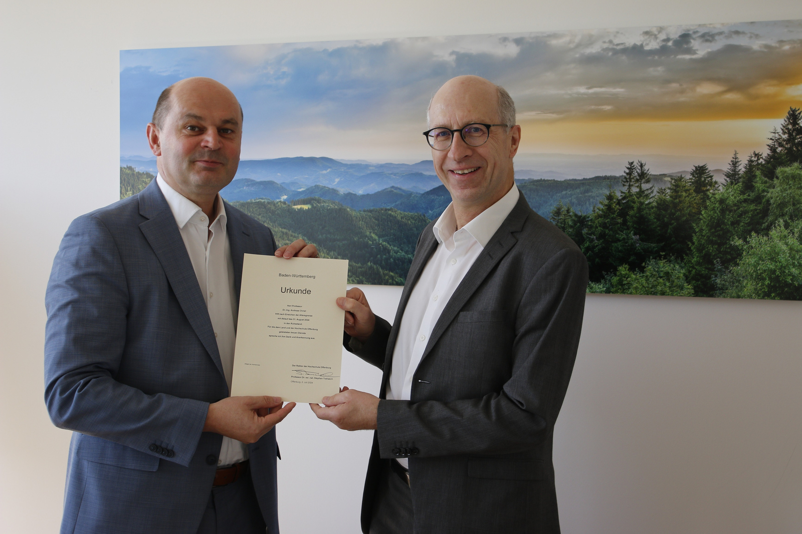 Die beiden Männer stehen vor einem Schwarzwaldfoto und halten die Urkunde in den Händen
