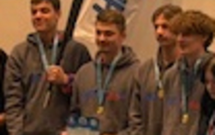 Vier junge Männer stehen bei der Preisverleihung mit Urkunden in der Hand auf einer Bühne, hinter ihnen die Teamfahne