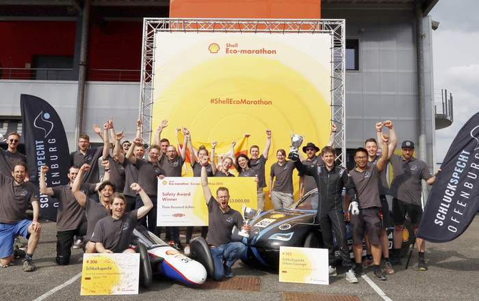 Jubelndes Team mit Siegerpokalen und -schecks sowie Fahrzeugen 