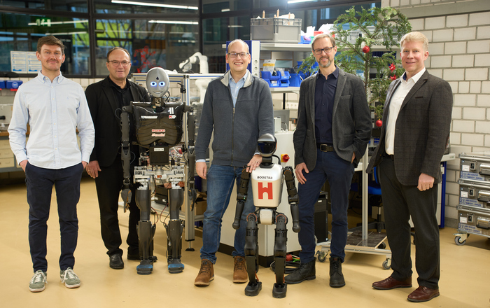 Fünf Männer stehen mit zwei humanoiden Robotern in einem weihnachtlich geschmückten Labor