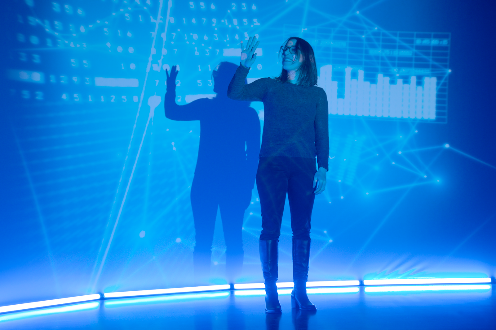 Eine junge Frau steht vor einem Bluescreen auf dem KI-Formeln zu erkennen sind und fährt mit der Hand darüber.