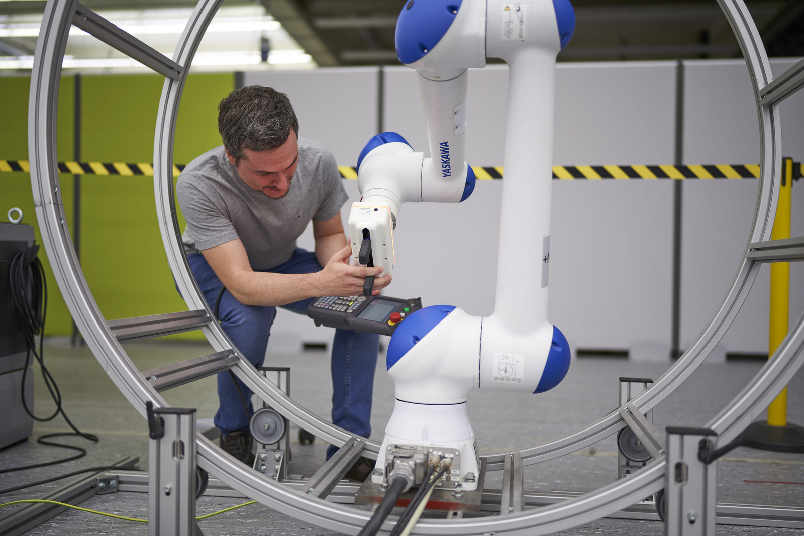 Ein Mann mit einer Elektroniksteuerung in der Hand arbeitet an einem Industrieroboter