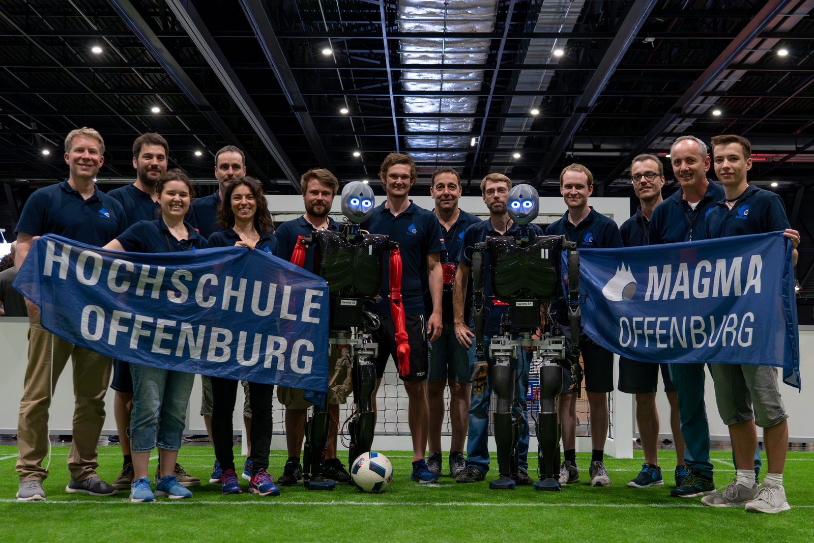 Gruppenfoto mit Hochschul- und Magma-Fahne und den Sweatys auf dem Platz