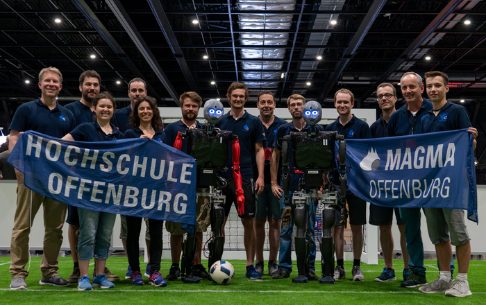 Gruppenfoto mit Hochschul- und Magma-Fahne und den Sweatys auf dem Platz
