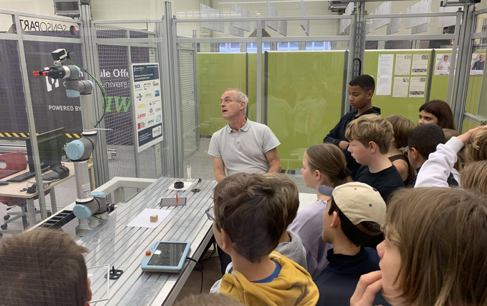 Ein Mitarbeiter zeigt einer Gruppe von Studenten einen Roboterarm