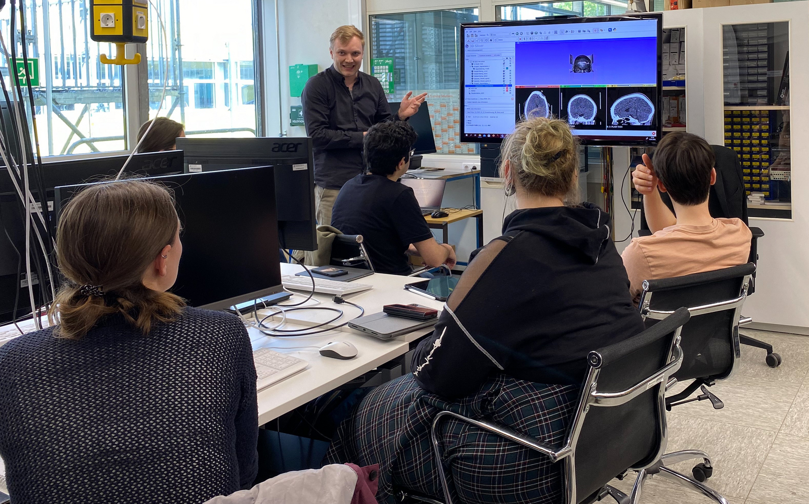 Wesley Dean Jones steht vor sitzenden Studierenden auf einem Bildschirm sind die CT-Aufnahmen eines Schädels zu erkennen