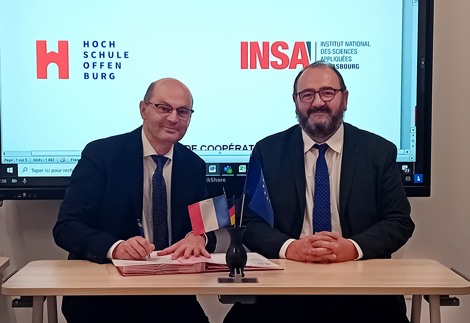 Zwei Männer sitzen an einem Tisch und unterzeichnen das Abkommen