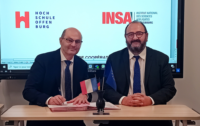 Zwei Männer sitzen an einem Tisch und unterzeichnen das Abkommen