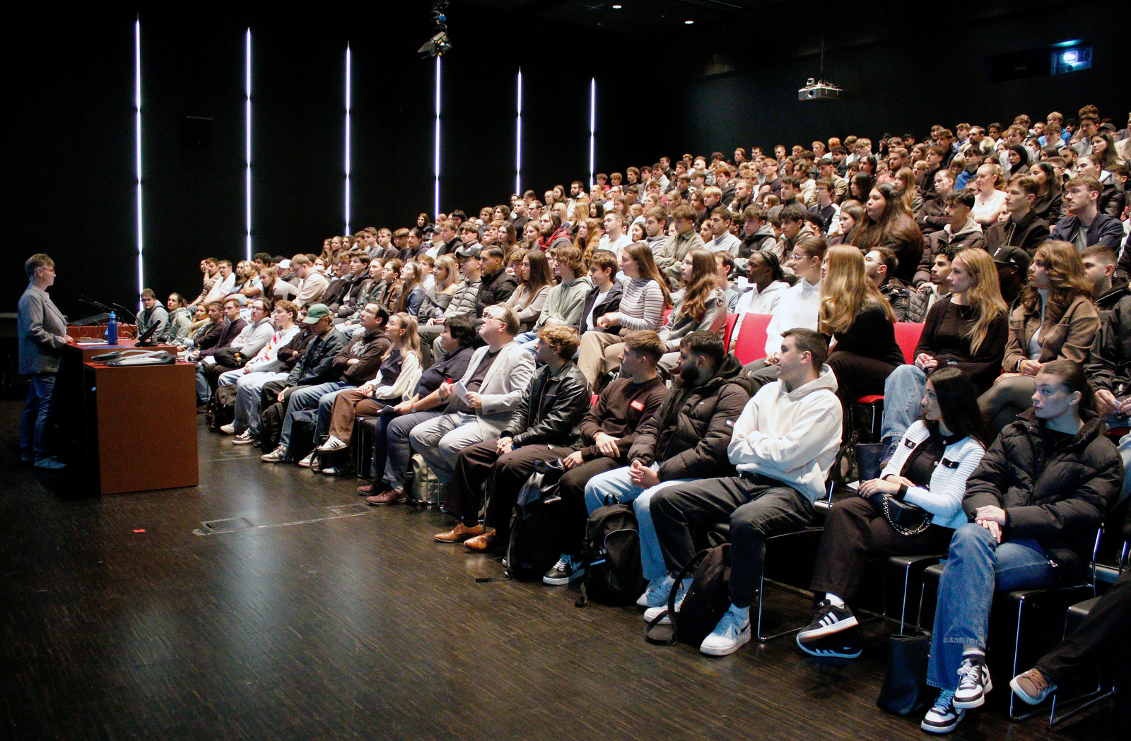 Eine Frau steht an einem rednerpult vor sitzenden Studierenden in einem Hörsaal.