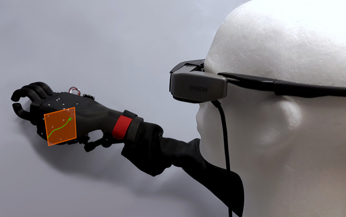 Ein Styroporkopf mit einer AR-Brille und eine Handprothese die an eine Wand greift 