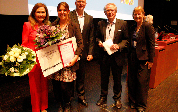 EinE gruppe von chic gekleideten Menschen zwei Frauen haben Blumensträuße in den Händen, die eine zusätzlich noch eine Urkunde und einen Scheck 