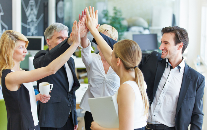 Fünf schick gekleidete Personen stehen im Kreis und geben sich ein High-Five.