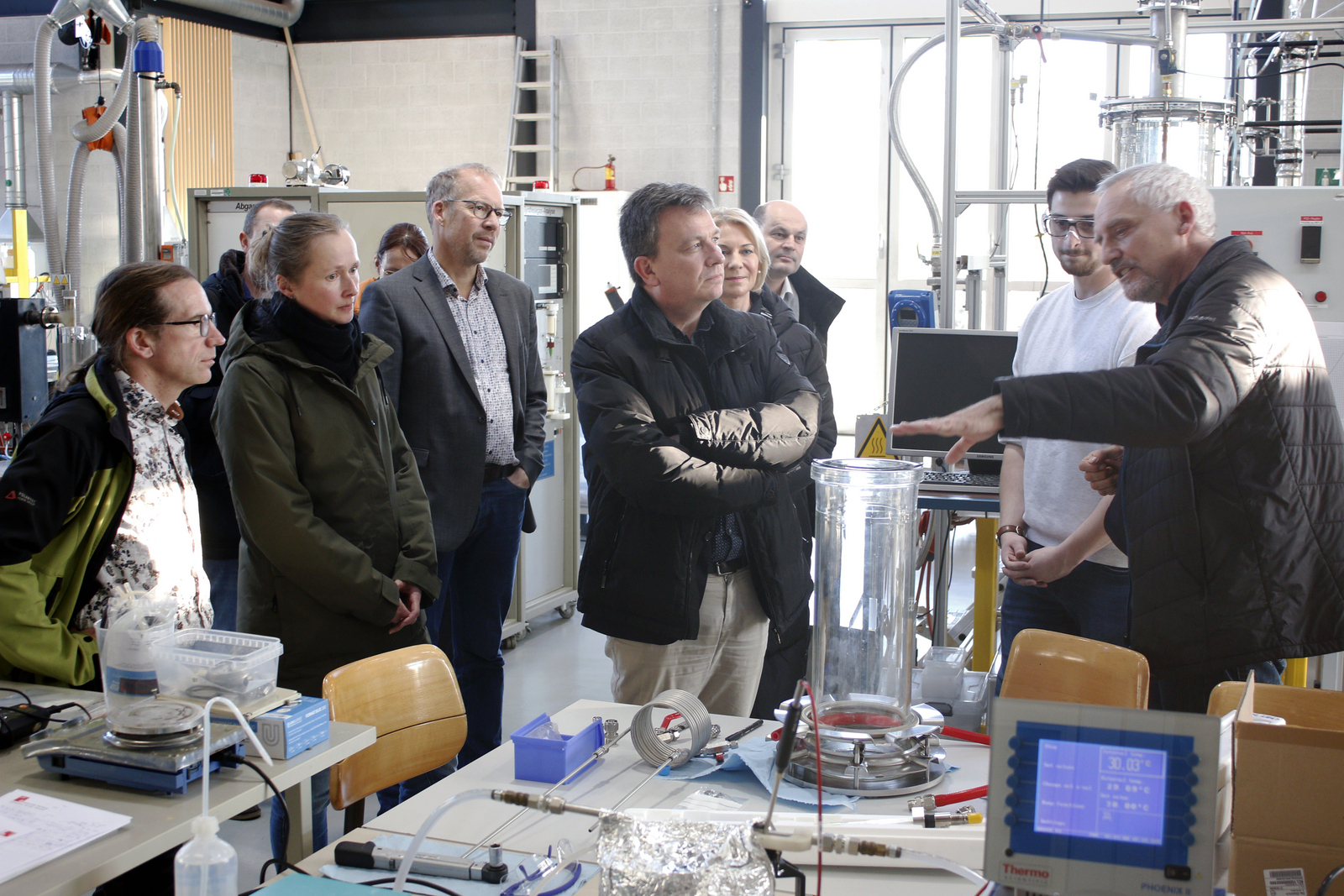 Ein Mann erklärt den anderen Kooperationspartnerinnen und -partner im Technikum etwas an einem Reaktor