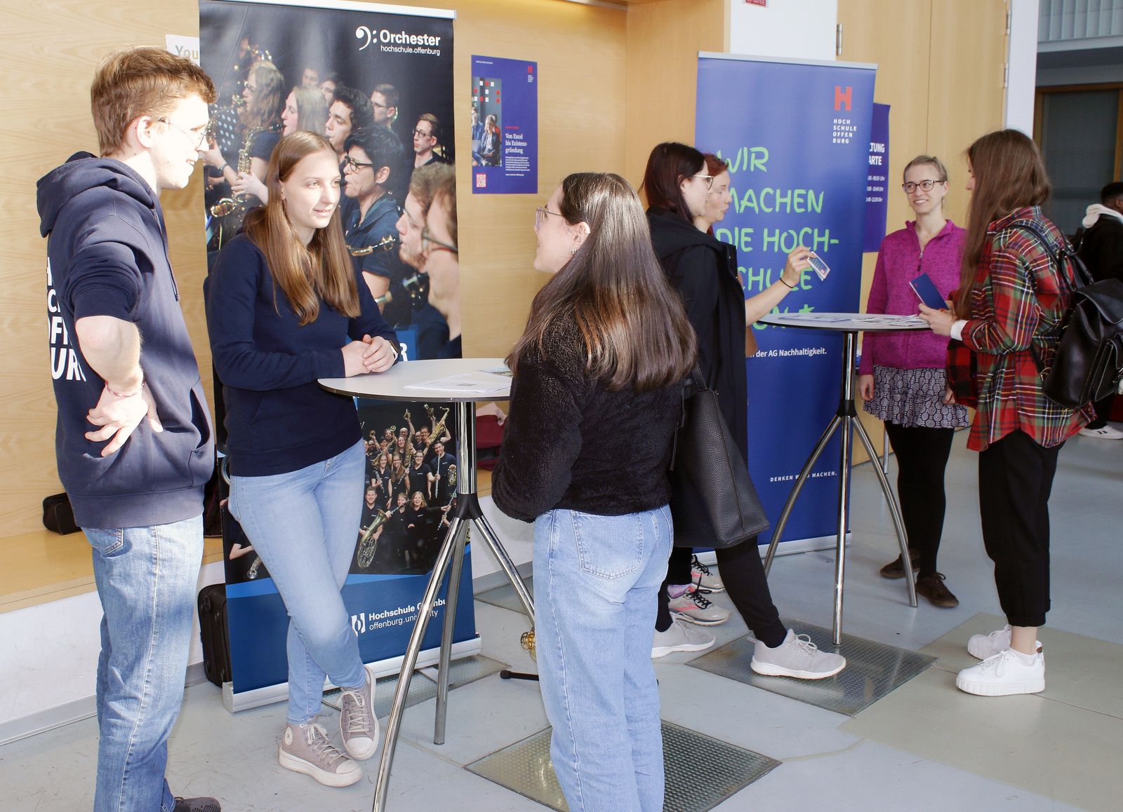 Junge Leute stehen vor Roll-Ups an Stehtischen 