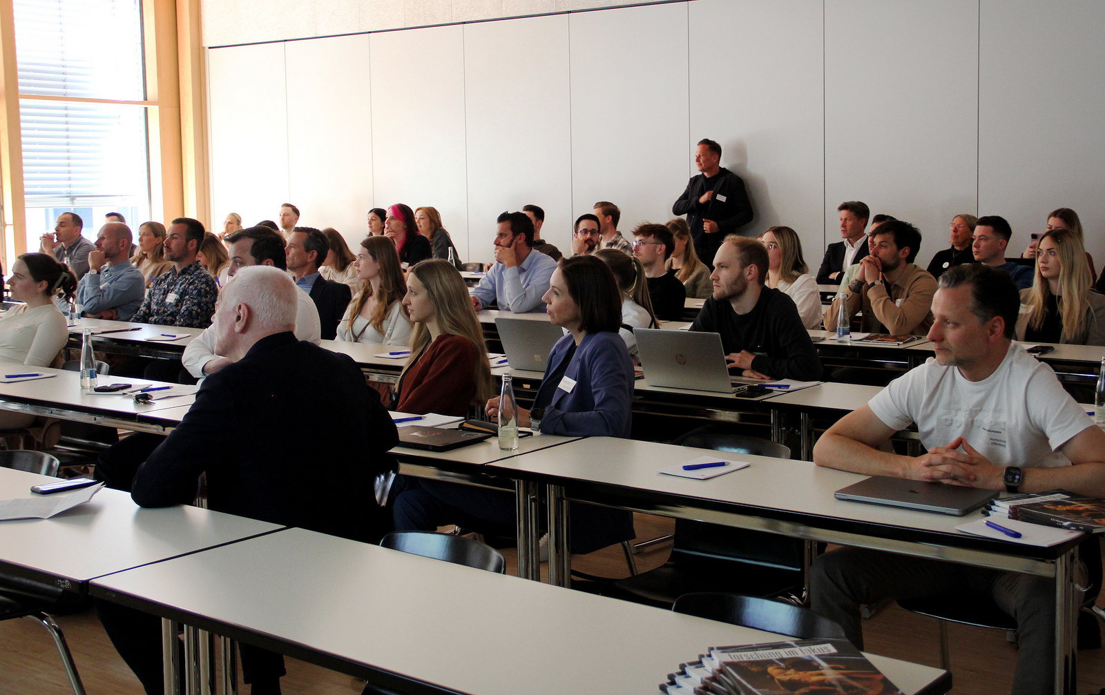 Das Publikum sitzt dichtgedrängt an Tischen im Hintergrund steht eine Person