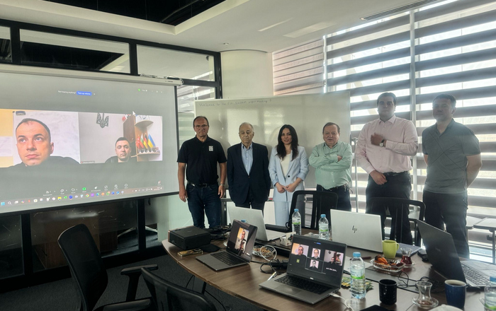 6 Personen in Reihe neben einer Leinwand mit 2 zugeschalteten Personen