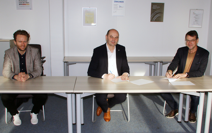 Christian Brunner, Ansprechpartner Studien- und Berufsberatung am Gymnasium der Klosterschulen, Hochschulrektor Prof. Dr. Stephan Trahasch und der Schulleiter der Klosterschulen OStD. Wilfried Arens (von links) sitzen bei der Unterzeichnung nebeneinander an Tischen.