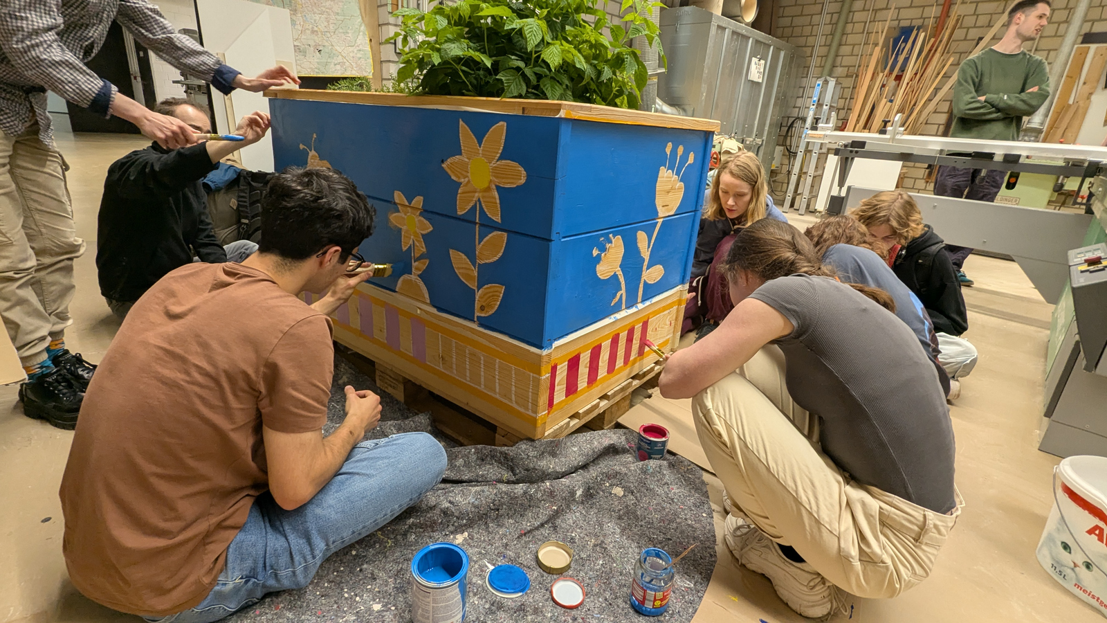 Junge Leute sitzen und stehen um ein Hochbeet herum und bemalen es