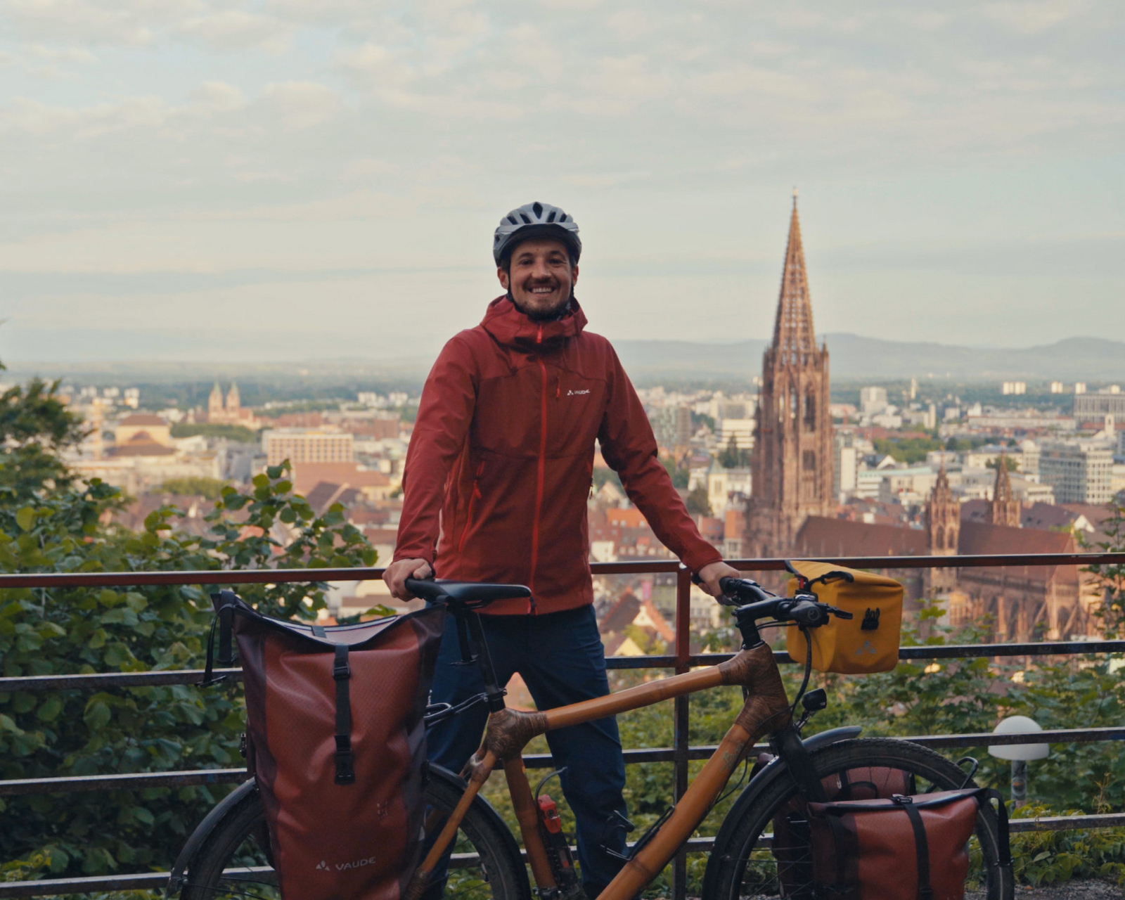 Ein Mann steht neben seinem Fahrrad auf einem kleine Berg hinter ihm im tiefergelegenen Tal ist das Freiburger Münster zu sehen