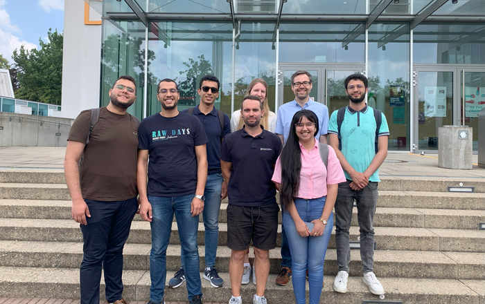 Fünf Studierende und ihre Betreuungsperson mit den DAAD-Referatsleitenden auf der Treppe vor dem D-Gebäude