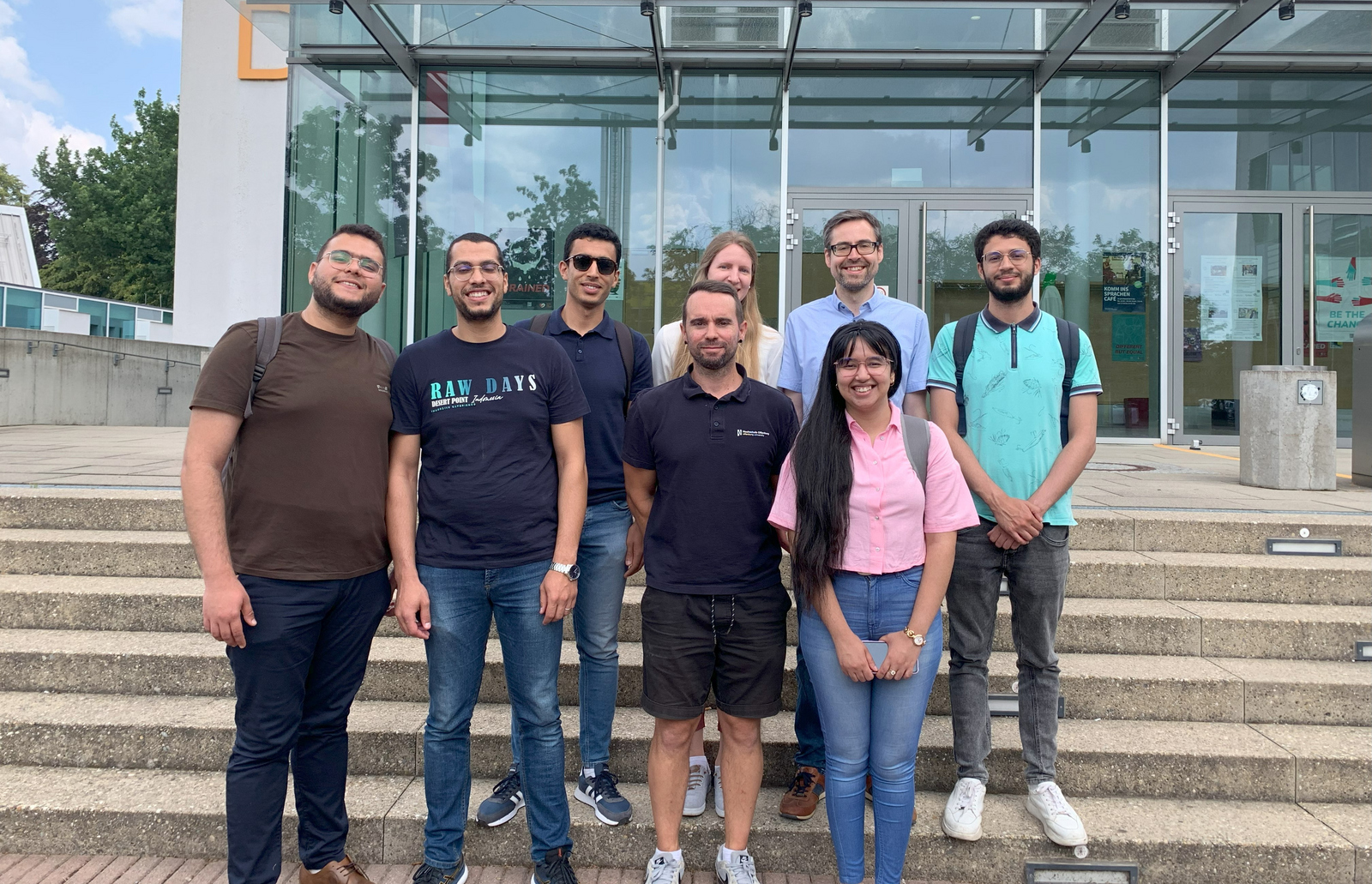 Fünf Studierende und ihre Betreuungsperson mit den DAAD-Referatsleitenden auf der Treppe vor dem D-Gebäude