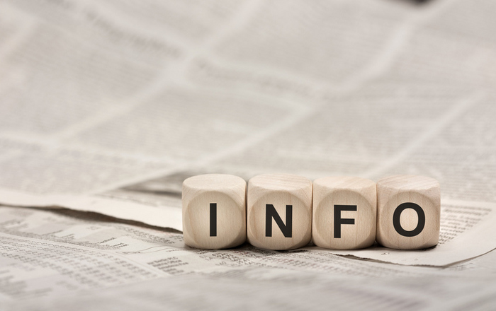 vier Würfel mit den Buchstaben INFO liegen auf einer Zeitung.