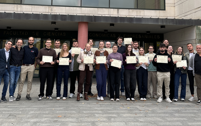 Eine Gruppe junger Menschen steht vor einem Universitätsgebäude und präsentiert ihre Zertifikate 