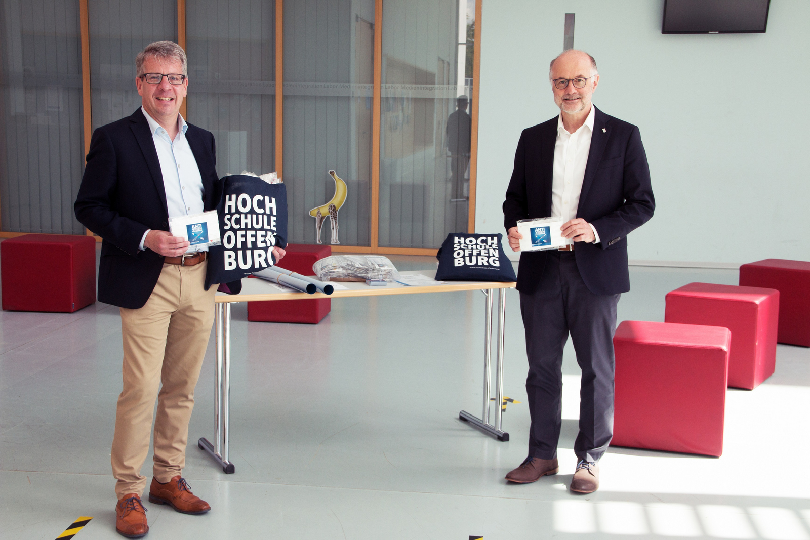 Rektor Prof. Dr. Winfried Lieber (rechts) übergibt Studiendirektor Martin Stern (links), dem stellvertretenden Schulleiter der kaufmännischen Schulen, Masken im Foyer des D-Gebäudes.