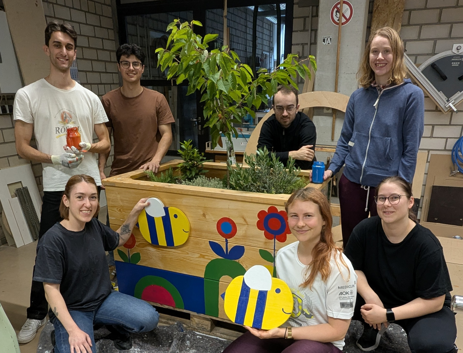 Junge Leute knien und stehen um ein bemaltes Hochbeet herum