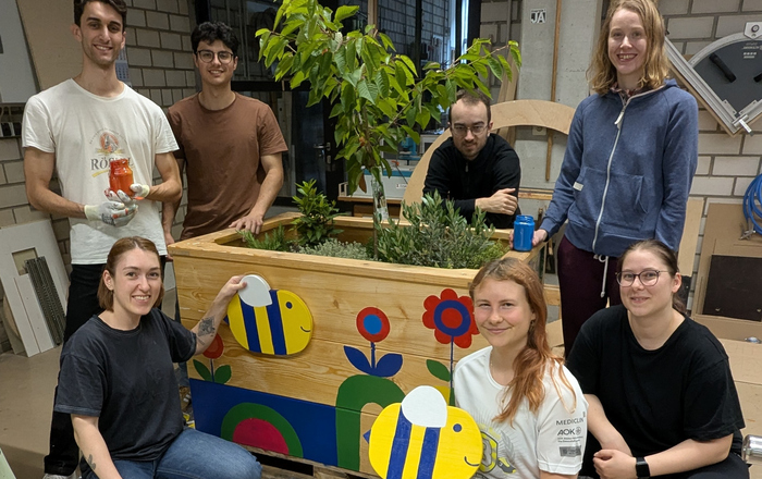 Junge Leute knien und stehen um ein bemaltes Hochbeet herum