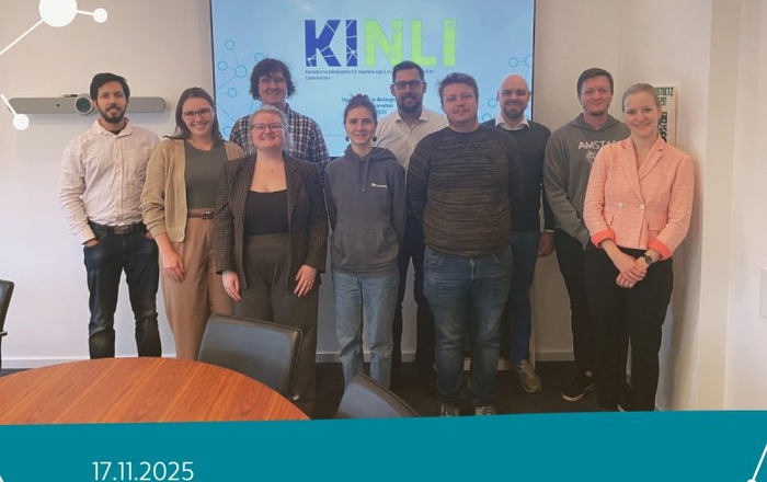 Gruppe von zehn Personen steht vor einem Bildschirm mit dem Schriftzug 'KINLI' in einem Besprechungsraum.