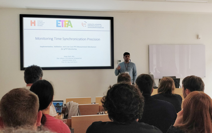 Raum mit Zuhörern 1 Person sthet vor einer Leinwand und präsentiert