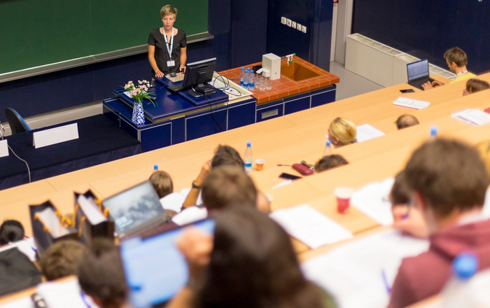 Eine Professorin steht in einem Hörsall vor Studierenden.
