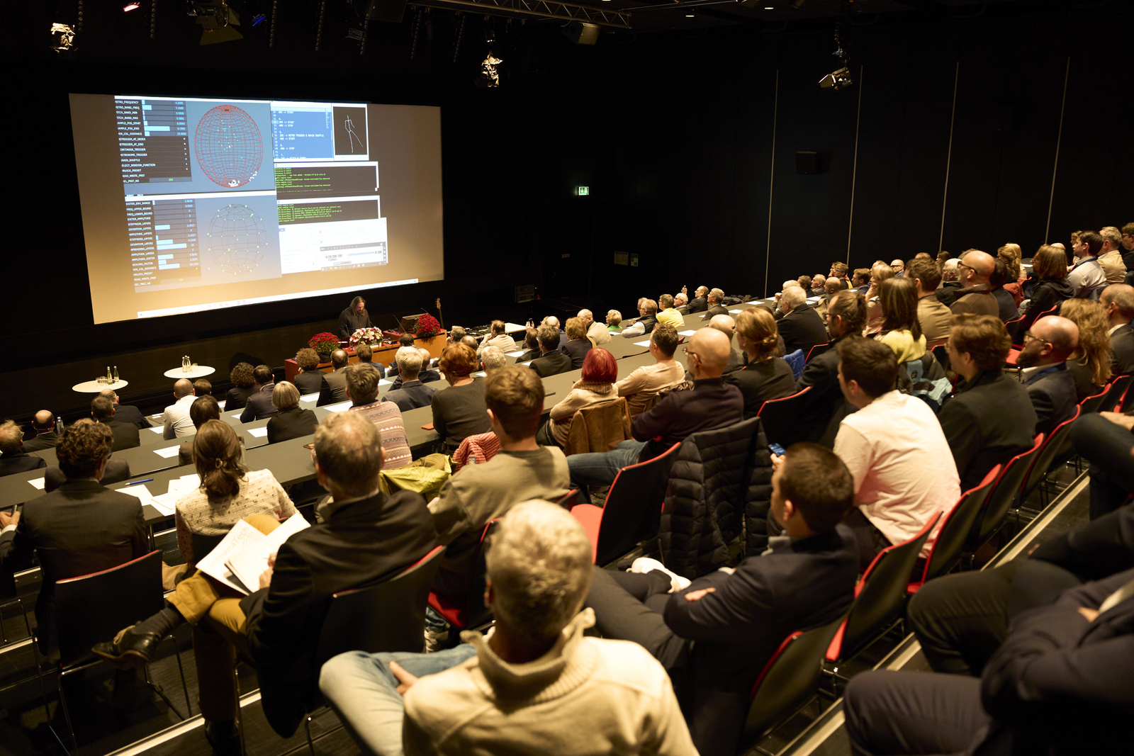 Blick über die sitzenden Gäste hinweg zum Rednerpulz und der Leinwand dahinter