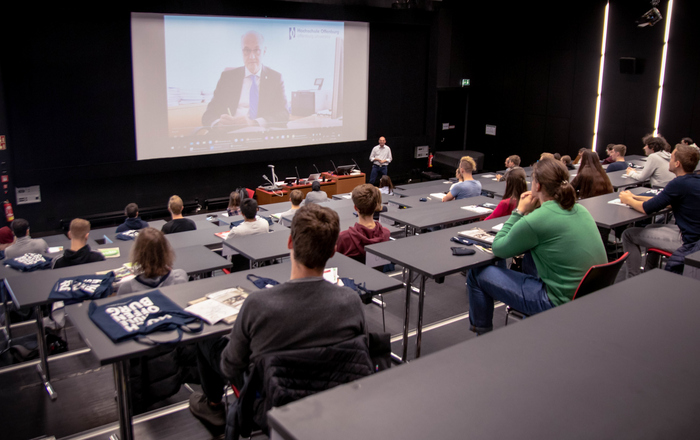 Hörsaal mit Erstsemestern zu denen Rektor Prof. Dr. Winfried Lieber von einer Videoleinwand spricht.