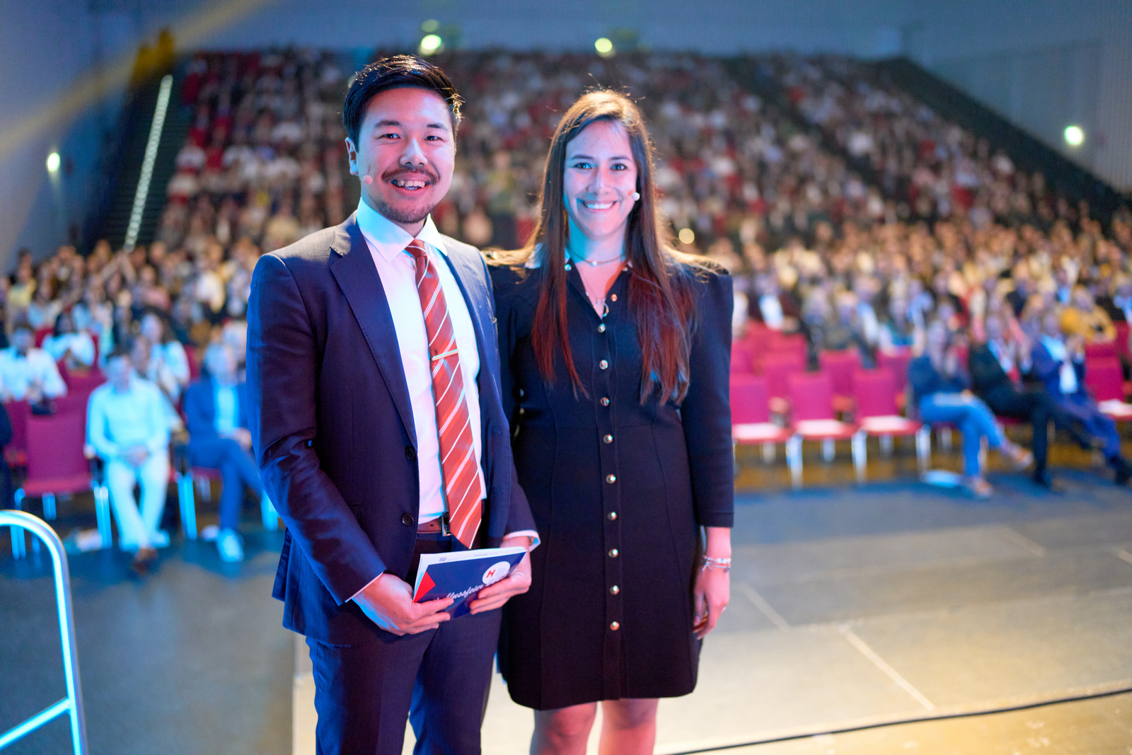 Ein Inder im Anzug und eine Mexikanerin im schwarzen Jackenkleid stehen nebeneinander mit dem Rücken zum Publikum